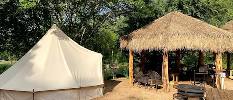 Una carpa, una estructura de paja y mesas de picnic en un camping.