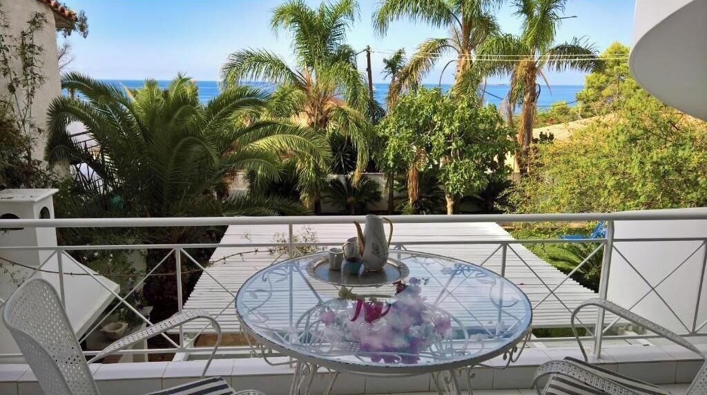 Ein Balkon mit einem Glastisch, Stühlen und Blick auf das Meer und Palmen.