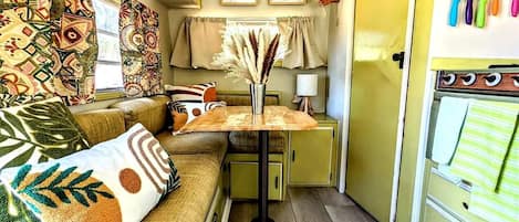 Interior de una caravana compacta con un sofá, una mesita y una pequeña cocina.