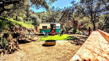Una casa móvil pequeña y colorida con un patio, una zona de fogata y una terraza de madera.