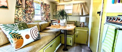 A compact kitchen with a dining area, a small table, and a sofa with cushions.