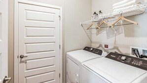 Un cuarto de lavandería con lavadora y secadora de carga frontal, una puerta blanca y un tendedero con perchas.
