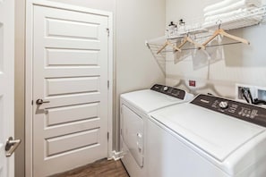 Une buanderie équipée d’un lave-linge et d’un sèche-linge à chargement frontal, d’une porte blanche et d’un étendoir à linge avec des cintres.