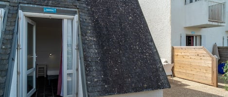 Um edifício com telhado inclinado, uma porta com a placa 'N114' e um portão de madeira.