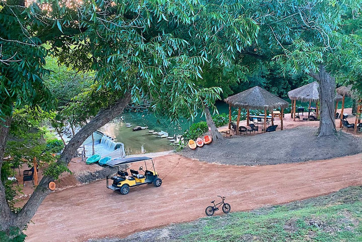 A paved path leading to a water feature with a small boat, a covered seating area, and a bicycle.