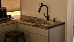 A compact kitchen with a single sink, a stool, and a microwave.