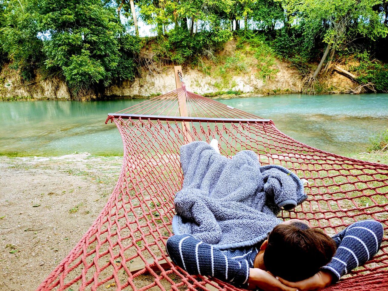A hammock tied between trees by a river, with a person lying in it.