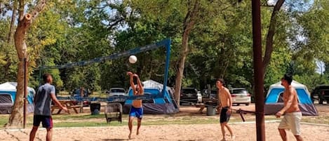 Una cancha de voleibol de arena con carpas al fondo.
