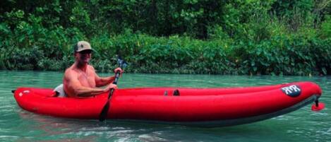 A person in a red kayak on calm water surrounded by dense greenery.