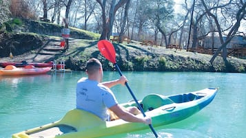 Une personne dans un kayak sur une rivière paisible, entourée d’arbres et de tables de pique-nique.