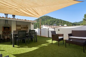 An outdoor patio with artificial grass, wicker furniture, a barbecue grill, and a view of a forested hill.