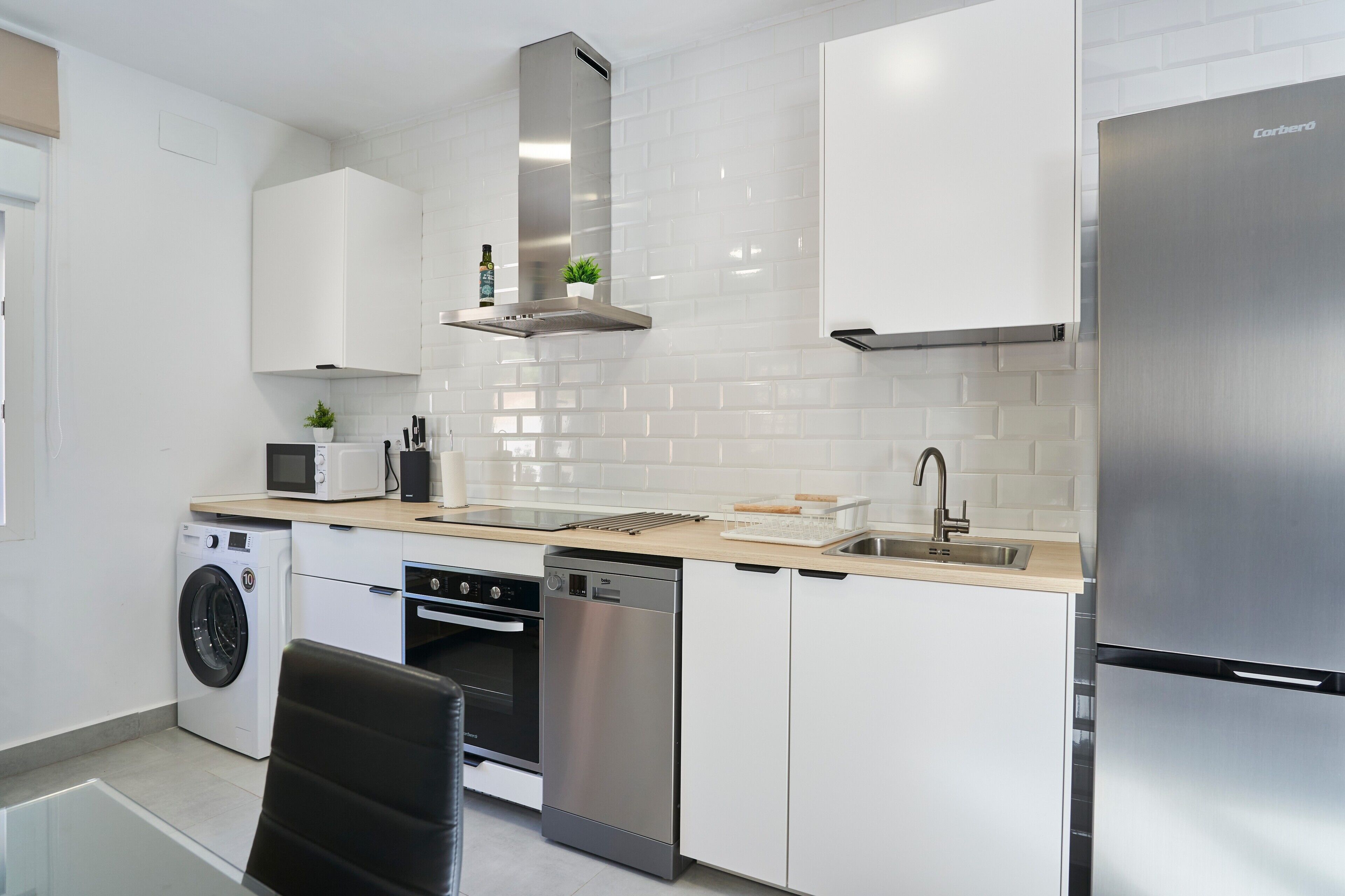 A modern kitchen with stainless steel appliances, white cabinetry, and a built-in dishwasher.