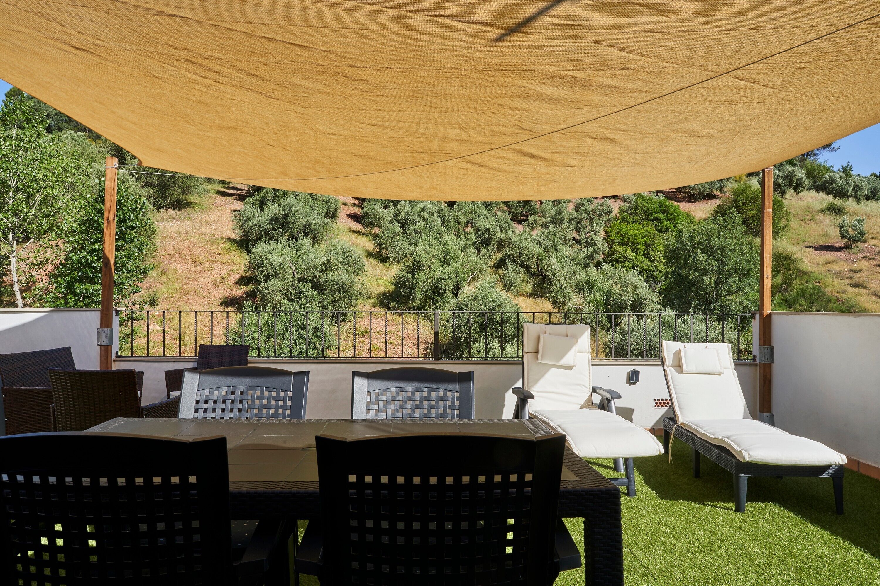 Un patio al aire libre con mesa y sillas, una tumbona y vistas a un paisaje montañoso.