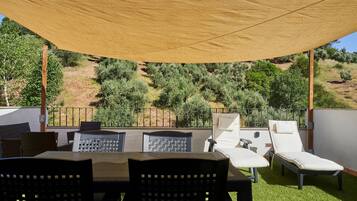 Un patio al aire libre con mesa y sillas, una tumbona y vistas a un paisaje montañoso.