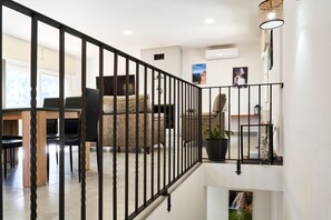 Una escalera con barandilla negra, un comedor con sillas y una mesa, y una planta en maceta en el rellano.