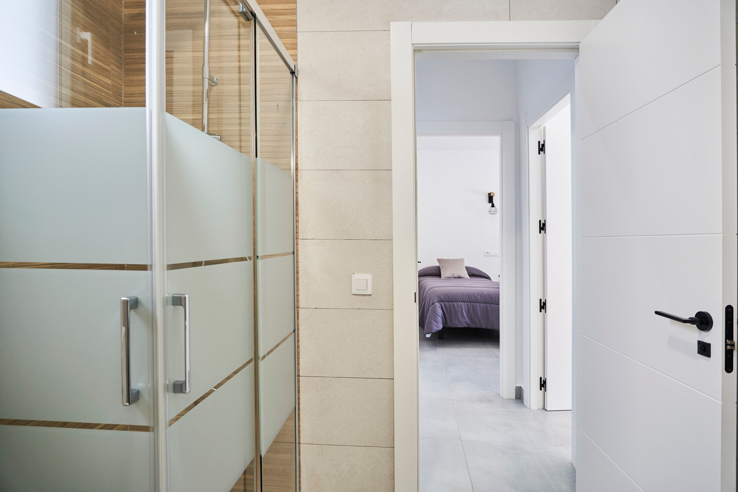Ein modernes Badezimmer mit Duschabtrennung aus Glas, einem weißen Schrank mit Griffen und einem sichtbaren Lichtschalter.