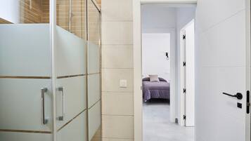 Ein modernes Badezimmer mit Duschabtrennung aus Glas, einem weißen Schrank mit Griffen und einem sichtbaren Lichtschalter.