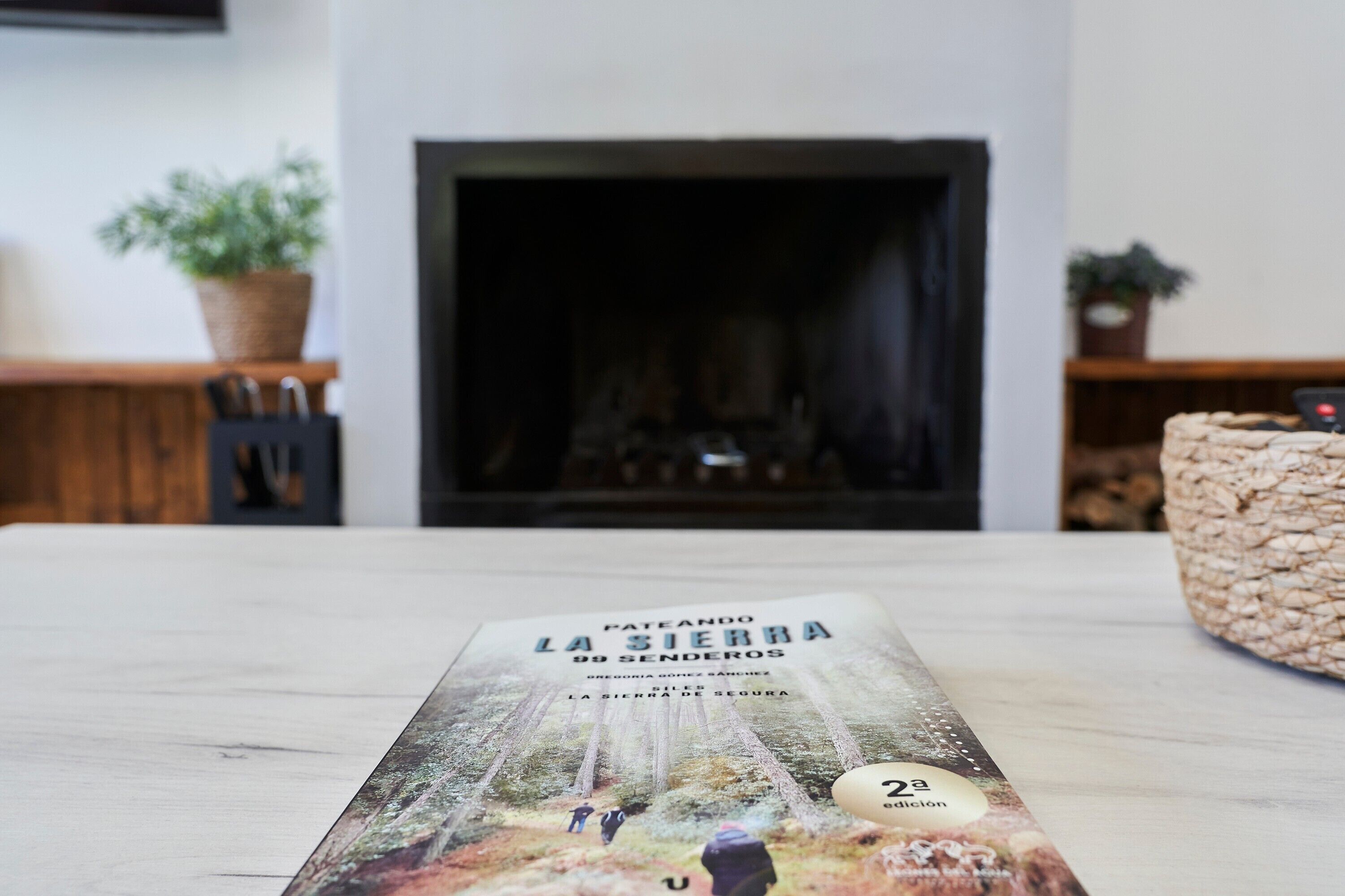 Een boek met de titel 'Pateando la Sierra 99 Senderos' op een tafel, met een open haard op de achtergrond.