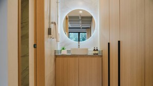A modern bathroom with a wooden vanity, a round mirror, and a window above the sink. - Modern 1BR in Juárez with fast WiFi, great natural light, a comfortable king bed, a fully equipped kitchen, and a luxury bathroom. Perfect for couples or solo travelers seeking comfort, style, and a prime location in Mexico City. (Cuauhtémoc)