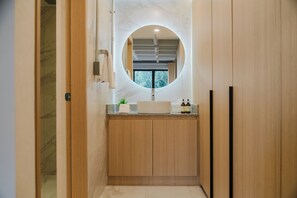 A modern bathroom with a wooden vanity, a round mirror, and a window above the sink. - Modern 1BR in Juárez with fast WiFi, great natural light, a comfortable king bed, a fully equipped kitchen, and a luxury bathroom. Perfect for couples or solo travelers seeking comfort, style, and a prime location in Mexico City. (Cuauhtémoc)