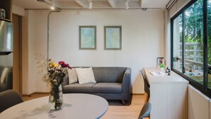 A modern living space with a gray sofa, a round table with a vase of flowers, and a small desk with a window view. - Modern 1BR in Juárez with fast WiFi, great natural light, a comfortable king bed, a fully equipped kitchen, and a luxury bathroom. Perfect for couples or solo travelers seeking comfort, style, and a prime location in Mexico City. (Cuauhtémoc)