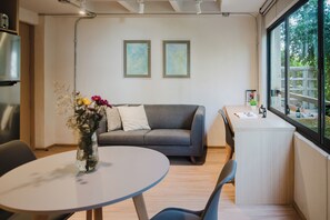 A modern living space with a gray sofa, a round table with a vase of flowers, and a small desk with a window view. - Modern 1BR in Juárez with fast WiFi, great natural light, a comfortable king bed, a fully equipped kitchen, and a luxury bathroom. Perfect for couples or solo travelers seeking comfort, style, and a prime location in Mexico City. (Cuauhtémoc)