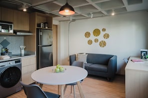 Eine moderne Küche mit Waschmaschine, einem Esstisch mit Äpfeln, einem grauen Sofa und einer Wand mit runden Dekorationen.