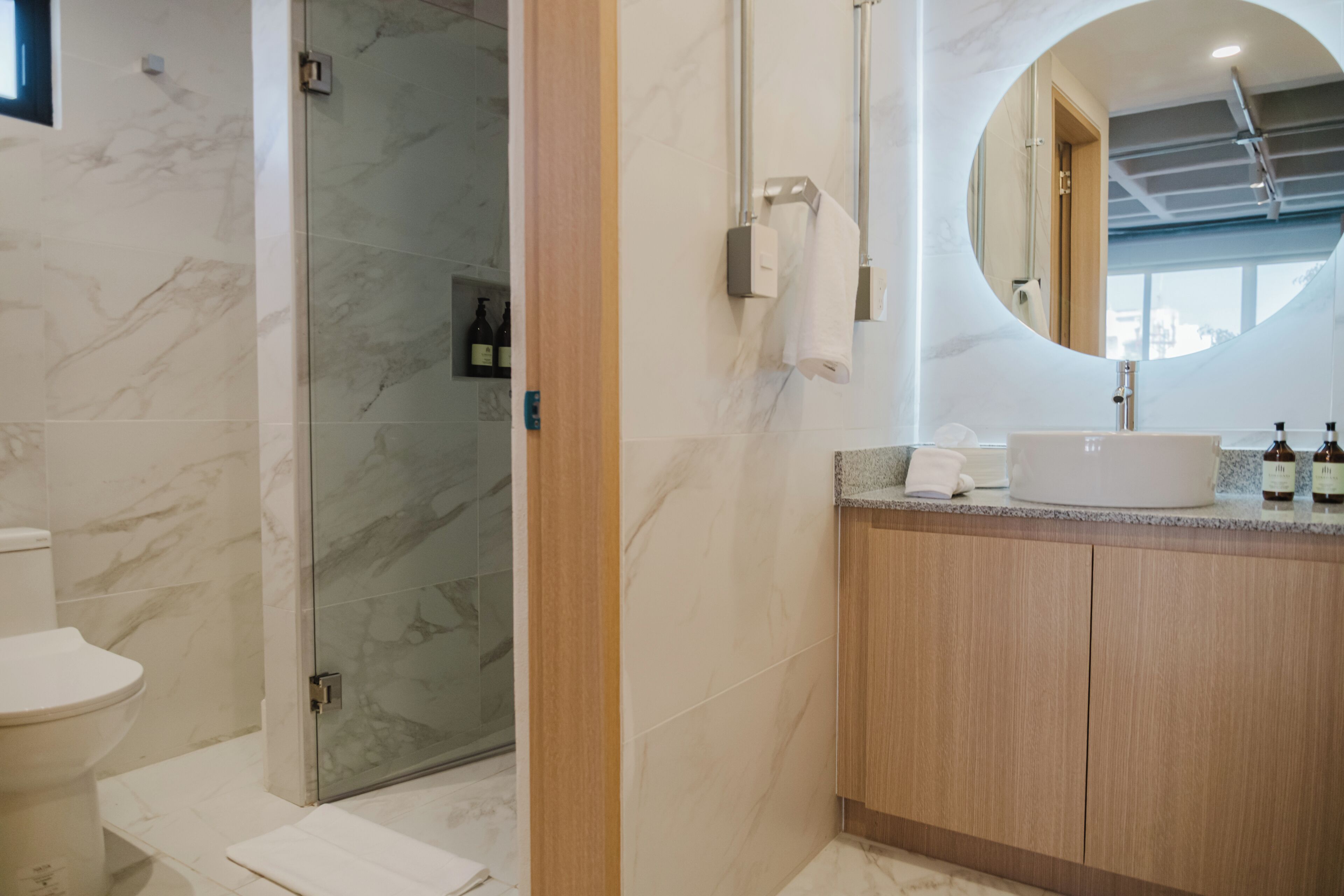 Een moderne badkamer met een douchecabine van glas, een houten wastafelmeubel en een ronde spiegel.