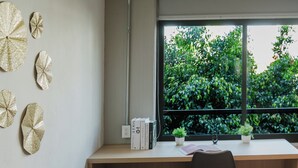 Ein modernes Zimmer mit grauem Sofa, einem Holztisch und einem Fenster mit Blick auf Grünflächen.