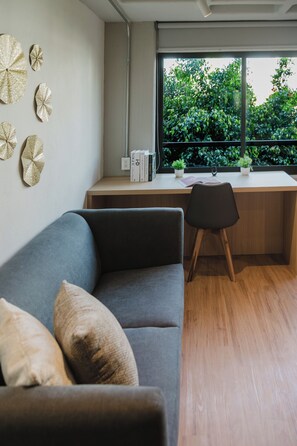 Ein modernes Zimmer mit grauem Sofa, einem Holztisch und einem Fenster mit Blick auf Grünflächen.