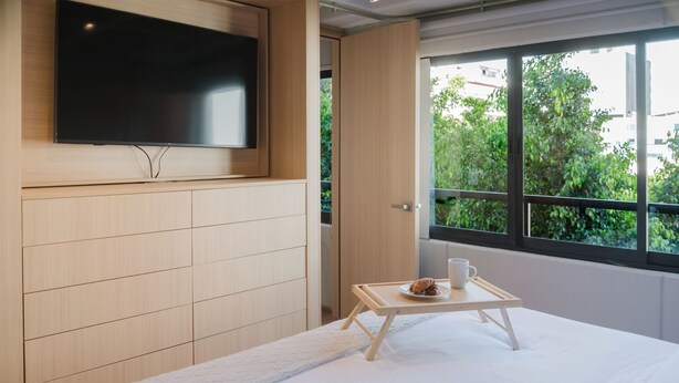 Ein modernes Hotelzimmer mit einem Bett, einem kleinen Tisch mit Tablett, einem Flachbildfernseher und einem Fenster mit Blick auf Grünflächen.