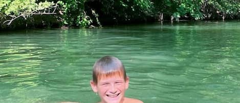 A person swimming in clear water with dense green foliage in the background.