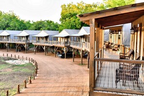 A row of wooden cabins with balconies, a dirt path, and a fenced area with chairs.