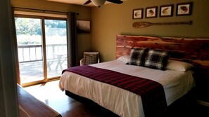 A bedroom with a large bed, a wooden headboard, a view of a deck through a sliding door, and a ceiling fan. - Arkansas River Paradise: Cabin with Large Deck Overlooking Breathtaking Views (Calico Rock)