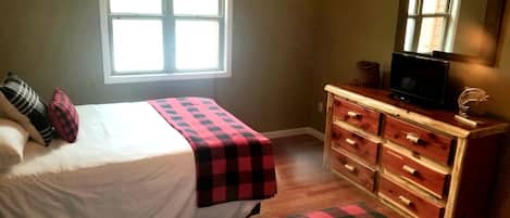 A bedroom with a bed, a dresser, a television, and a window.