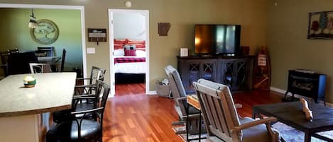 Un soggiorno con TV, zona pranzo con sedie, angolo cottura con tavolo e sedie, e una porta con l'indicazione 'River House'.