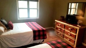 Un dormitorio con una cama, un aparador, un televisor y una ventana.