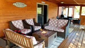 Un porche de madera con muebles de mimbre, una fogata y un letrero que dice 'Bienvenido a nuestro porche'.
