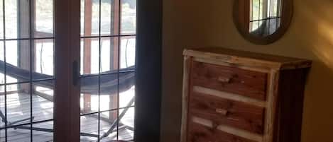 Una habitación con un aparador de madera, un espejo redondo en la pared y vistas a través de una ventana con celosía de metal.