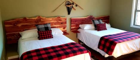 Duas camas de solteiro com cabeceiras de madeira, roupa de cama branca e cobertores quadriculados pretos e vermelhos.