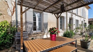A wooden table with a metal frame, a red potted plant, and a pergola structure. - Charming Gîte in Périgord for 2 to 6 Guests (Saint-Martin-de-Gurson)