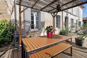 A wooden table with a metal frame, a red potted plant, and a pergola structure.