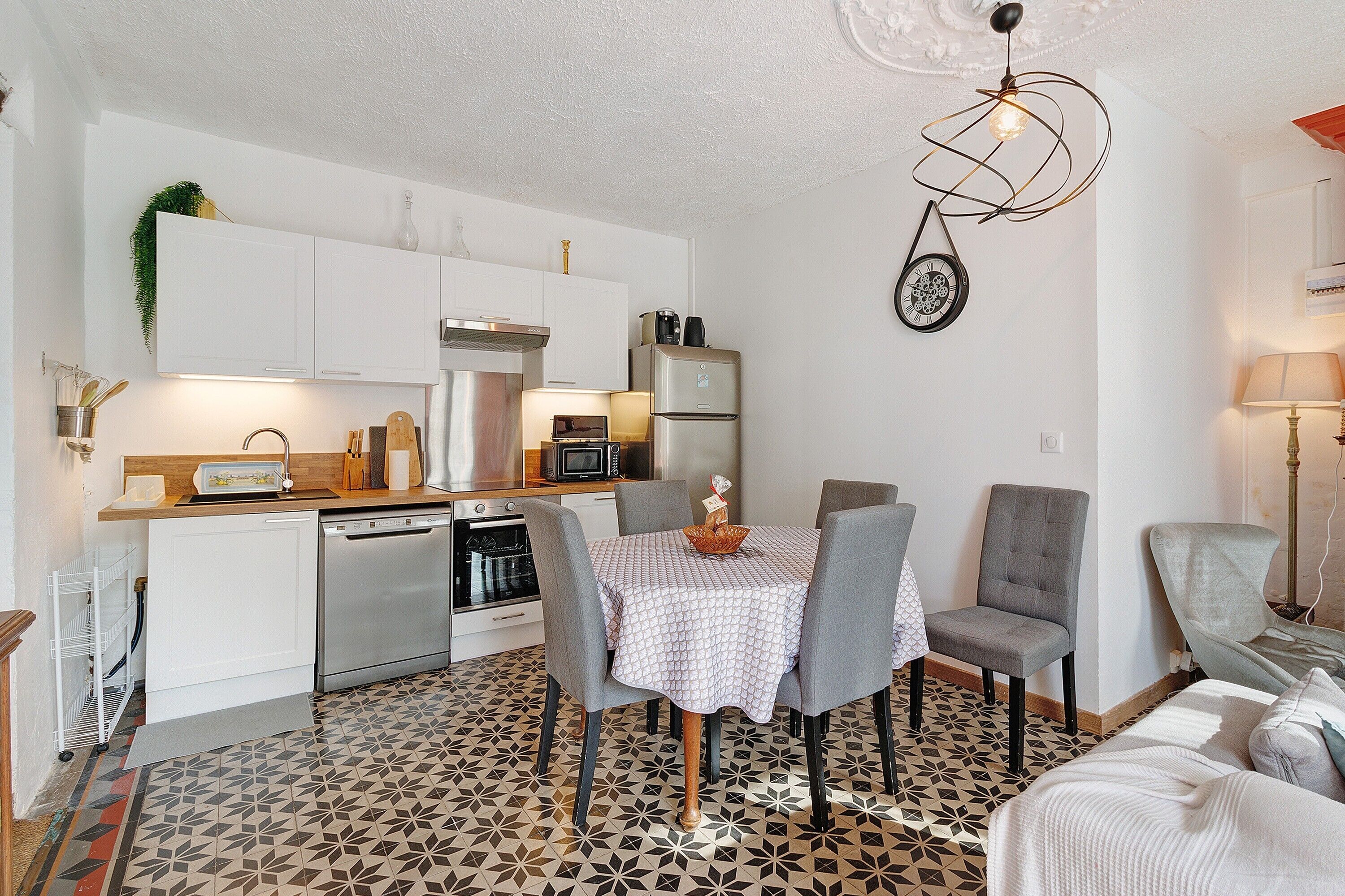 Een kleine keuken met witte kasten, een eettafel met vier stoelen en een vloer met een patroon.