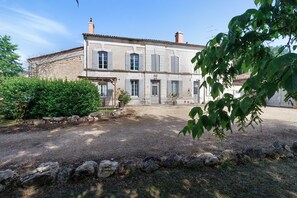 A two-story building with a stone facade, multiple windows, and a gravel driveway.