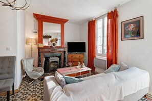 Um quarto com lareira, televisão, sofá, poltrona e cama.