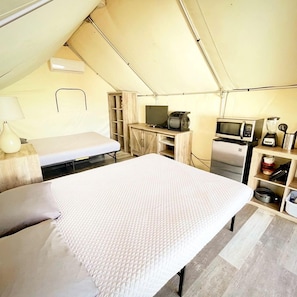 A tented accommodation with a bed, a television, a microwave, and a small kitchenette. - Exciting Family Glamping Getaway by the San Marcos River: Charming Safari Tent near Kingsbury, Texas (Kingsbury)