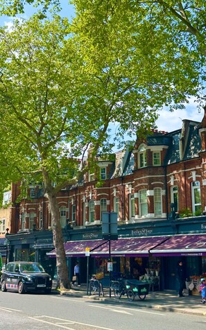 A row of brick buildings with storefronts, including a bakery and a pharmacy. - Charming London Apartment in Chelsea/ Fulham (London)