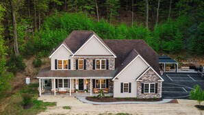 A two-story house with a stone facade, a covered porch, and a driveway leading to a parking area.