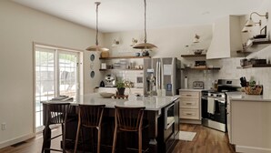 A modern kitchen with a central island, bar stools, stainless steel appliances, and pendant lighting.