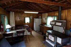 A rustic cabin with a wooden interior, a dining table with chairs, a kitchenette with a stove, and a refrigerator. - Simple, Pet Friendly Country Cabin in Poudre Canyon, Colorado (Bellvue)
